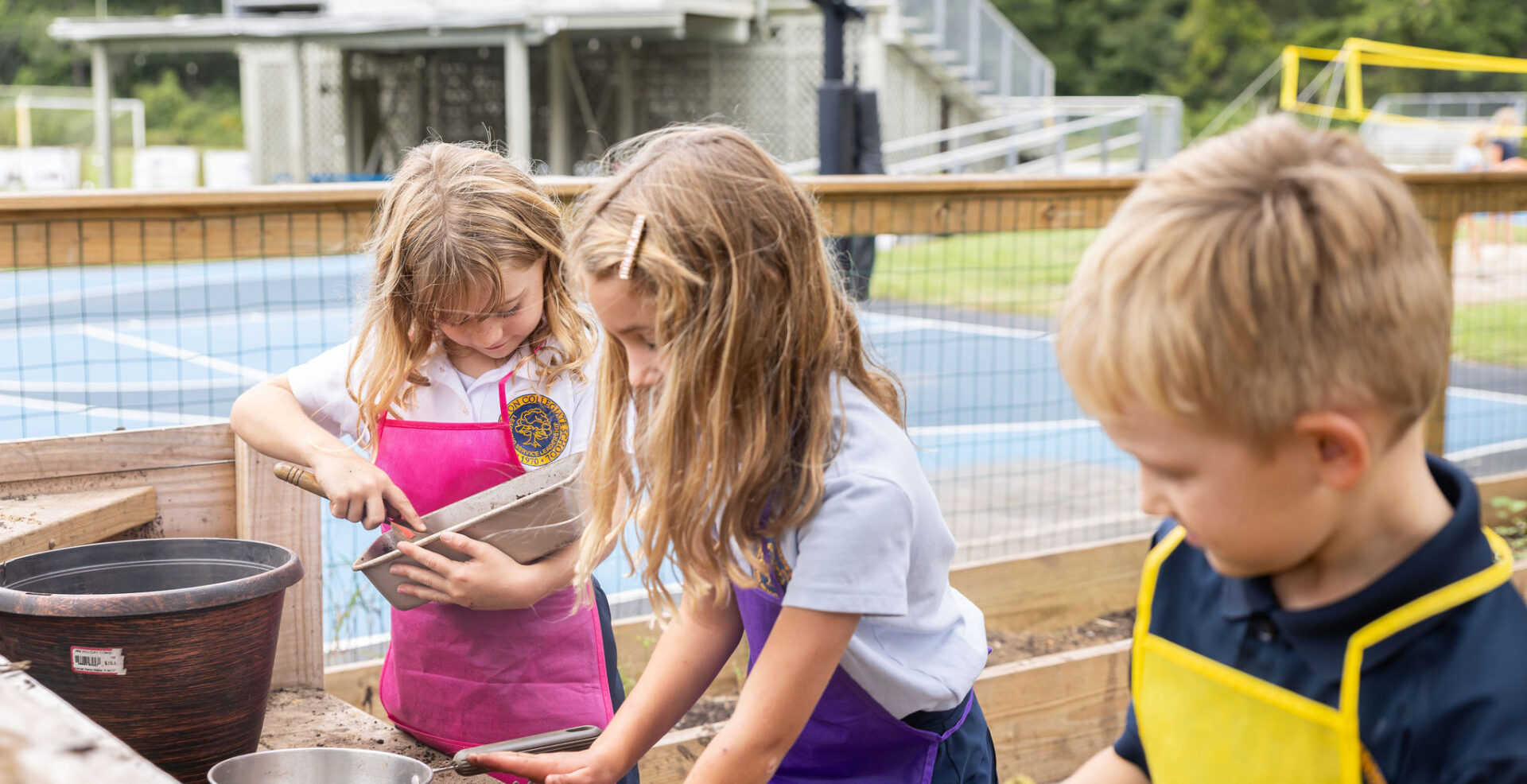Students wearing aprons and playing in the mud kitchen area of the on campus garden.
