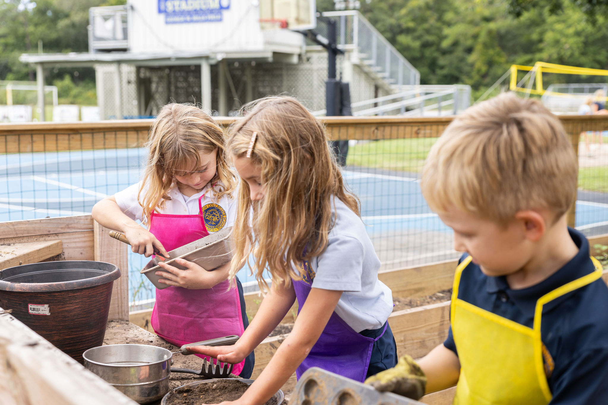 Students wearing aprons and playing in the mud kitchen area of the on campus garden.