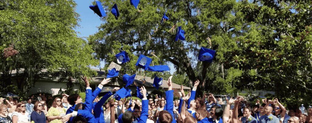 Seniors throwing their caps into the air during outdoor graduation under the live oak trees.