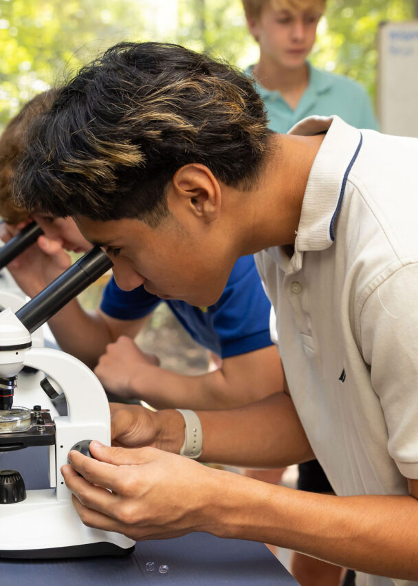 Upper schoolers use a microscope in the outdoor education center. 