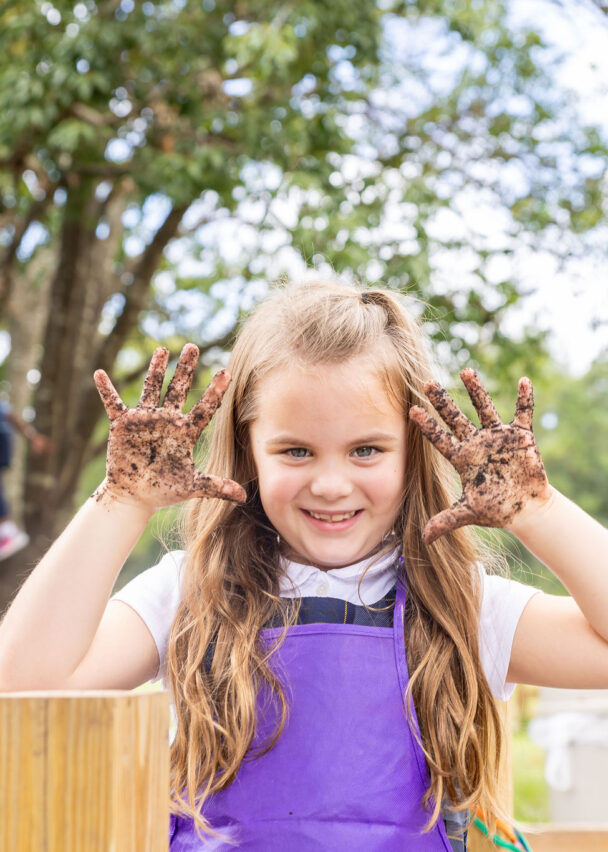 A student gets their hands dirty while gardening in the outdoor classroom.